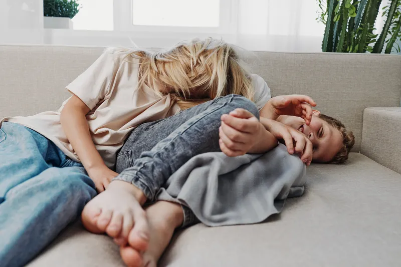 Playful mother and child lying on sofa in casual clothes, laughing and enjoying tender moment at home. Concept of family bonding, joy, and relaxed lifestyle.