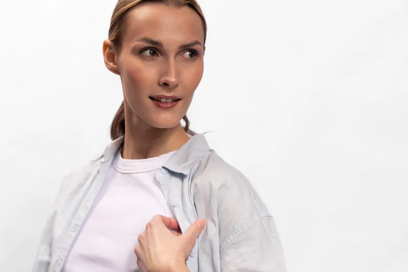 Young woman with light hair wearing casual white shirt and t-shirt looks aside thoughtfully. Portrait on white background with soft lighting and natural expression for lifestyle concept.