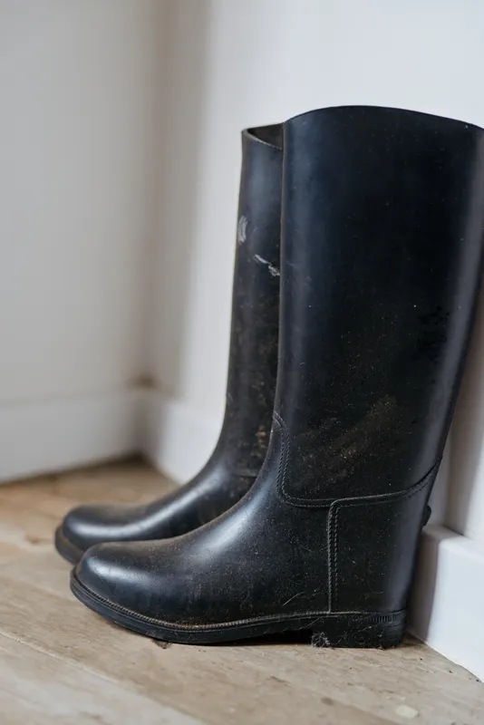 Close view of a pair of black boots standing by a white wall indoors, everyday footwear ready for errands, simple home lifestyle with muted tones, soft light and calm atmosphere
