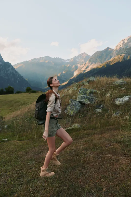 Young woman with long hair and a backpack hikes through a mountain meadow enjoying the fresh air and natural landscape during a sunny day.