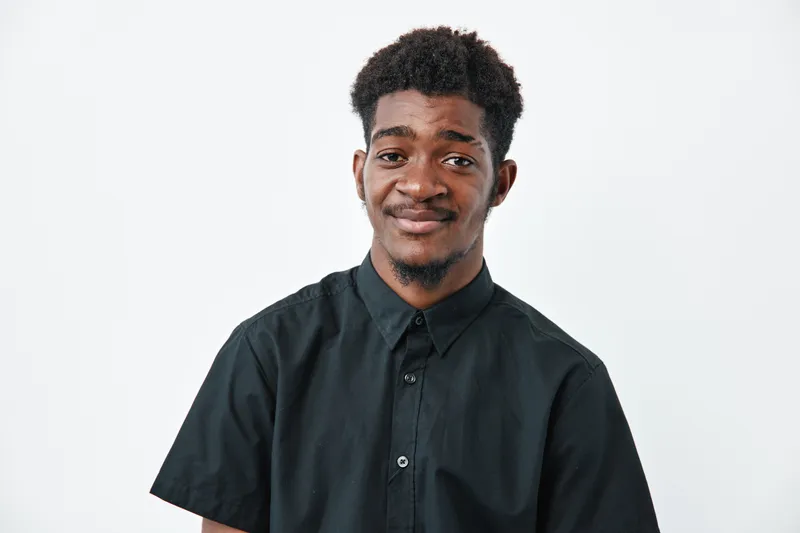 Young black man with dark skin and curly hair wearing black shirt smiling and looking at camera on white background. Portrait of confident african ethnicity male with casual style.