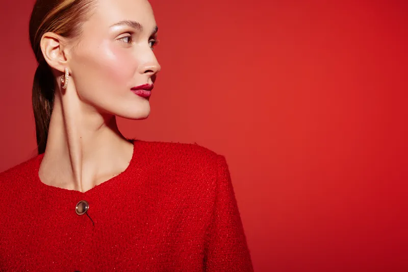 Elegant woman with red hair and red lipstick wearing a red textured jacket looks sideways on a red background. Concept of fashion, beauty, and style with monochrome tones.