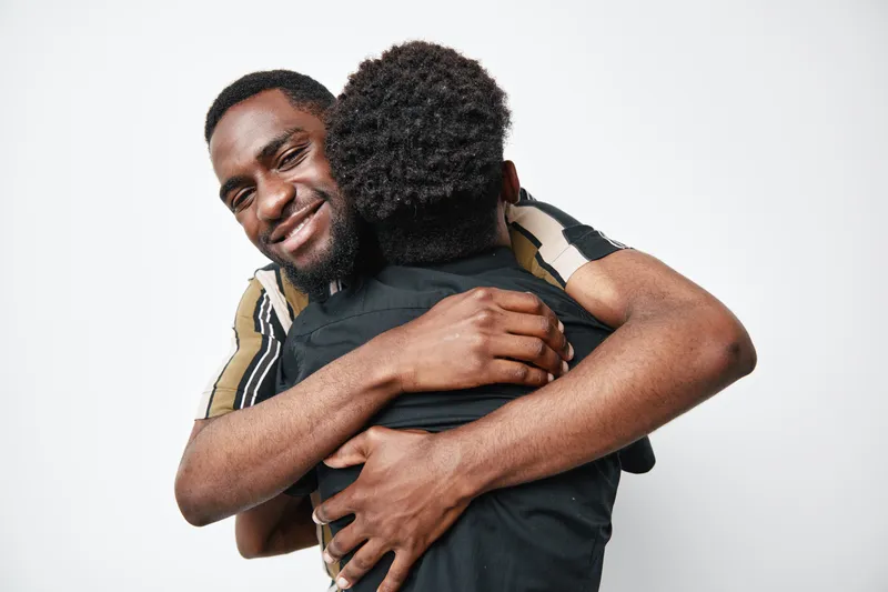 Two African American men with dark skin hugging each other in friendly embrace on white background. Happy black men showing affection and connection with smile and casual clothes.