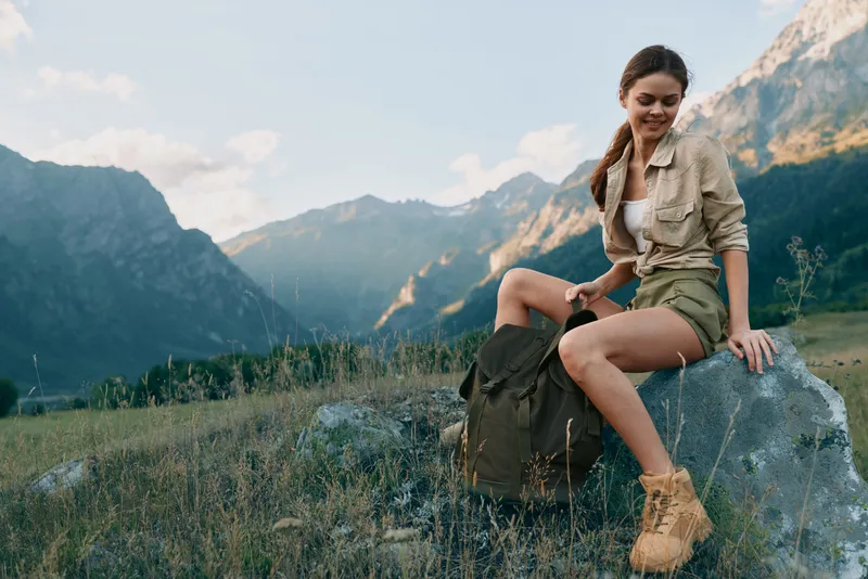 Cheerful woman outdoors, hiking in mountains, casual outfit, sunlit moment, relaxed pose, natural colors, fresh air, nature backdrop, scenic landscape in warm light