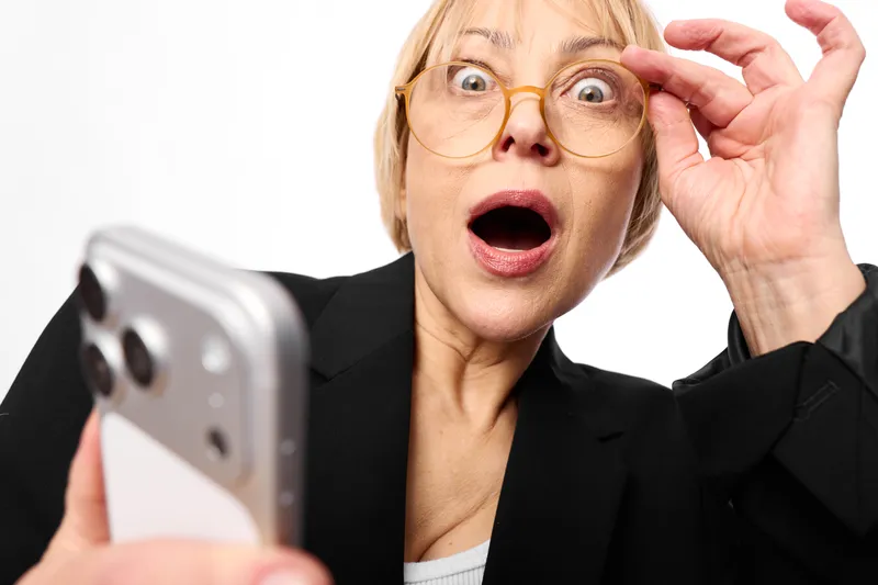 Woman surprised and shocked, holding glasses and phone in business suit, wide open mouth, stunned expression in studio, digital communication for social media news