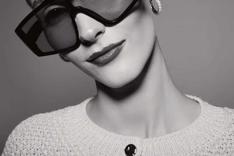 Close-up of a stylish white woman with fair skin wearing large black sunglasses and a knit sweater. Portrait shows elegance, fashion, and modern accessories in studio lighting.