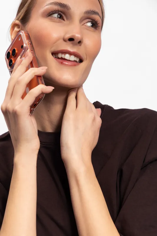 Smiling young woman in brown sweater holding smartphone near ear, looking aside with joyful expression. Concept of communication, technology, happiness, and casual lifestyle on white background.