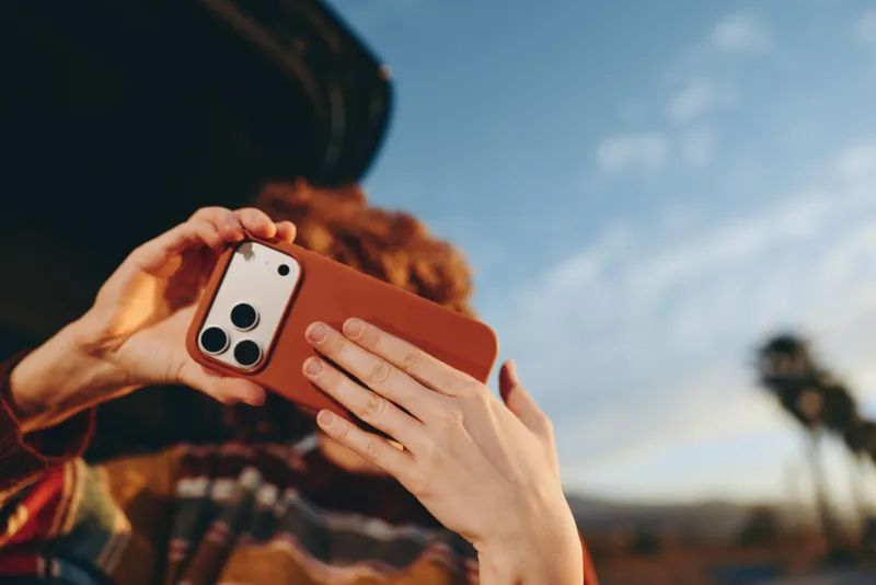 Woman lifestyle outdoors, smartphone in hands as she takes a photo, portrait moment with curly hair, warm clothing, bright sky, communication and personal content in nature today