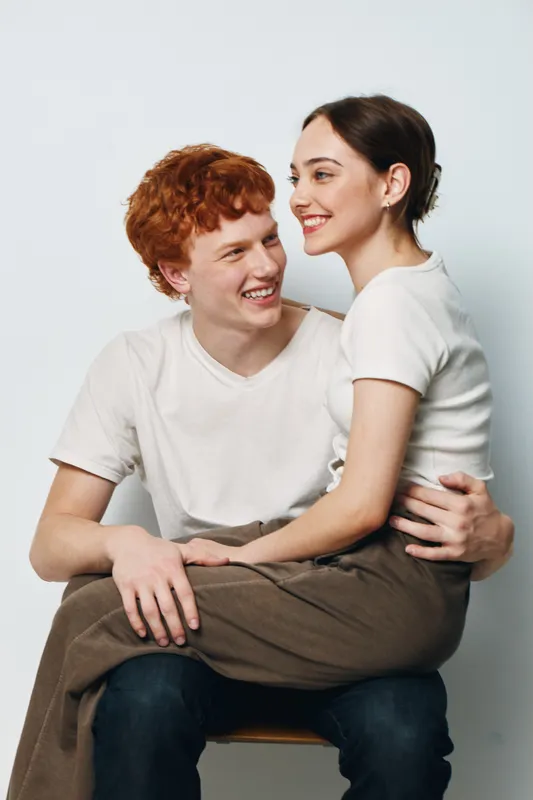 Couple, young man and woman sitting closely together smiling with affection and joy in casual clothes on plain background. Relationship, love and happiness concept with friendship.
