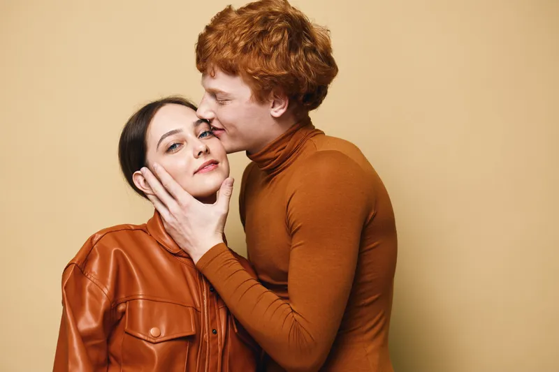 Couple, love and affection with man kissing woman on cheek, emotional connection and romance in studio. Young people with tender moment and closeup portrait on beige background for relationship.