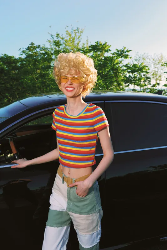 Joyful woman lifestyle retro film color outdoor car sunny fashion portrait, candid moment with denim shorts striped top, curly hair and bright smile, conveying freedom and happiness