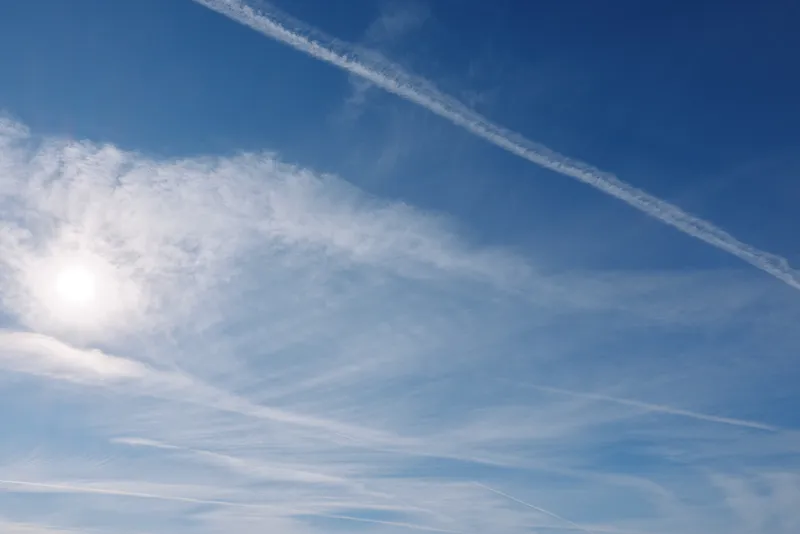 Sky blue contrails sun clouds wide open atmosphere in a clear expanse, conveying calm and travel potential in vast daylight sky