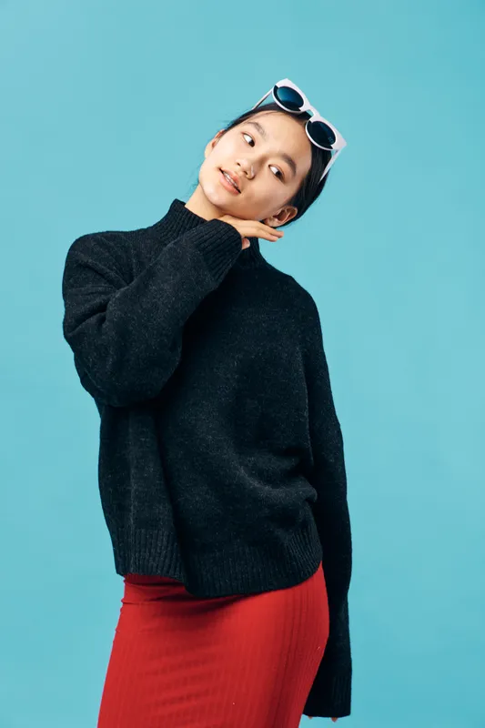Young woman in black sweater and red skirt poses with sunglasses on head against blue background. Casual fashion, confident model and stylish outfit for modern look and beauty portrait.