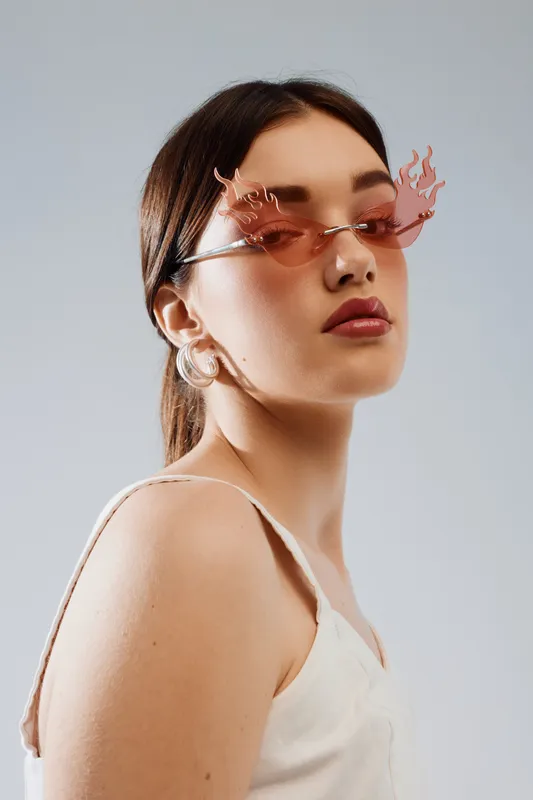 Young woman in stylish pink sunglasses and white top poses confidently against a neutral background. Concept of beauty, fashion, and modern accessories for lifestyle.