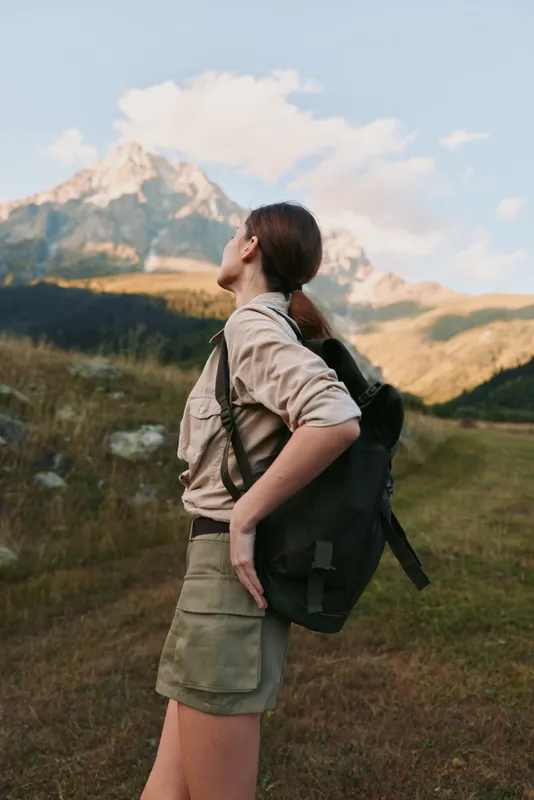 Young woman with a backpack gazes toward distant mountains on a hiking trail, feeling curious, confident, and empowered as nature surrounds her.