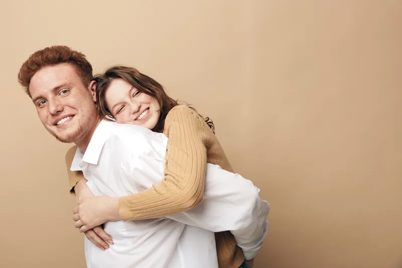 Happy young couple embraces and smiles in casual clothes on beige background. Concept of love, relationship, friendship, and positive emotions between man and woman.
