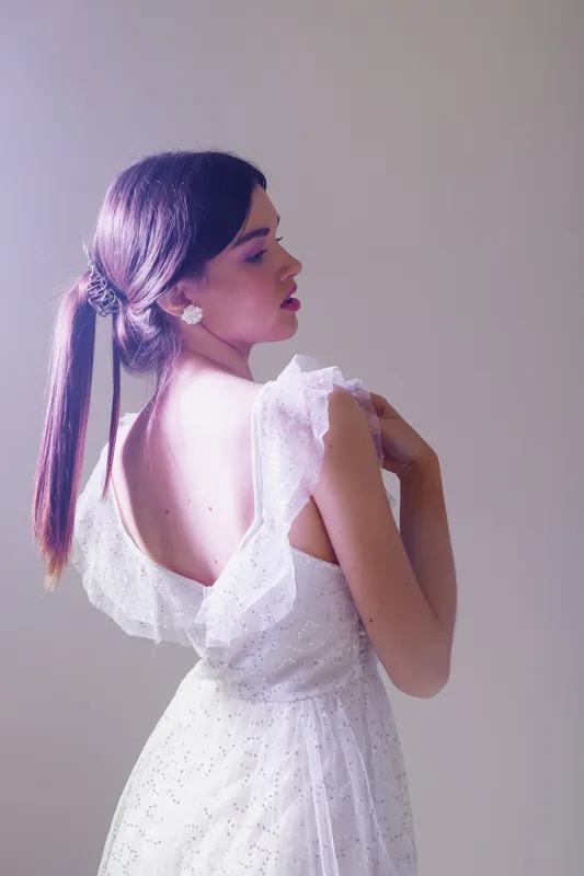 Young woman in a white lace dress poses with her back turned, showcasing elegance and beauty. Soft lighting highlights her smooth skin and delicate fashion details. Concept of woman beauty fashion.