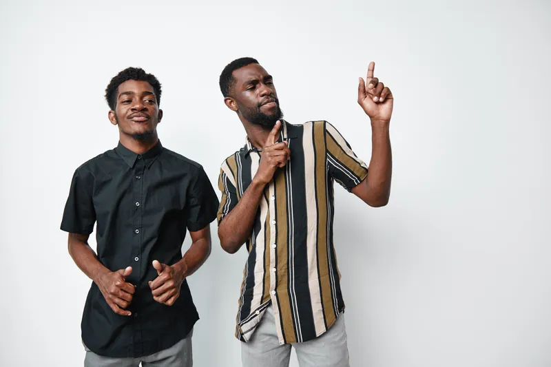 Two african men with dark skin posing and smiling on white background. Casual clothing, standing close, happy expression and relaxed mood in studio photo.