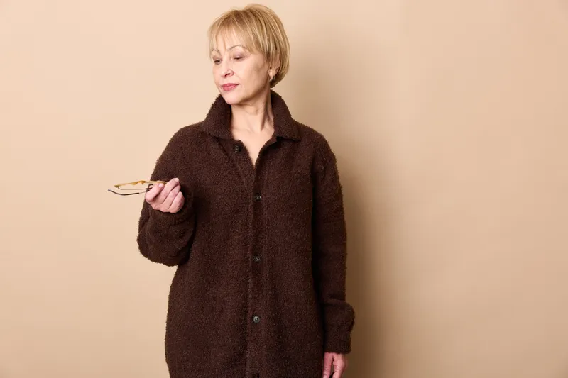 Woman money holding counting elderly worried beige portrait, mature female in dark coat checks cash bills, indoor finance stress concept on plain background