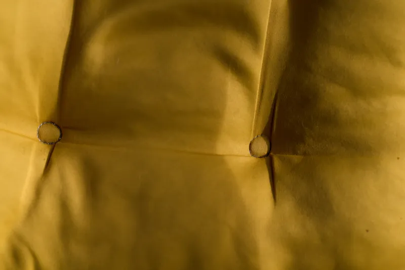 Close-up of yellow fabric with stitched seams and round buttons, showcasing texture and minimalistic fashion detail with warm, tactile mood