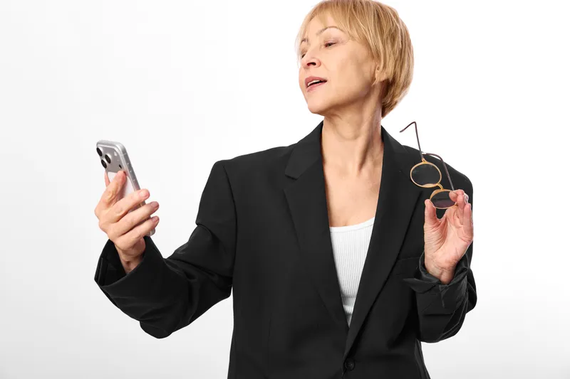 Businesswoman uses smartphone and phone to present credit card for payment, online shopping, digital commerce concept, isolated on white background, black blazer confident portrait