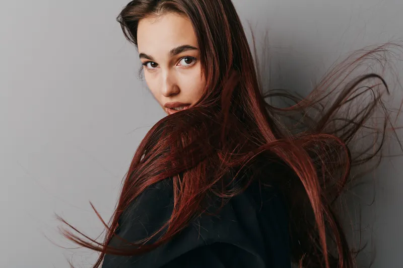Woman with long brown hair wearing black clothing posing with hair flowing and serious expression on gray background in studio. Fashion, beauty and portrait concept with natural look and style.