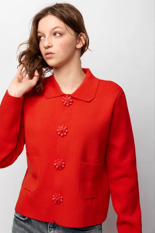 Young woman in red knitted cardigan with decorative buttons looks away thoughtfully. Casual fashion, autumn style, portrait on white background with natural expression.