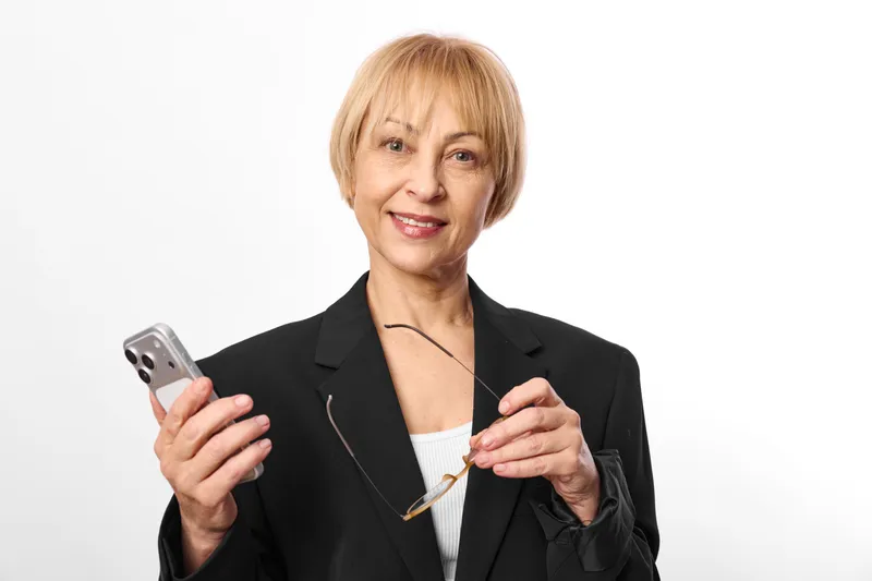 Smiling elderly woman holding a smartphone and touching the screen, studio portrait on white background, concept of communication, technology, connection, everyday mobile
