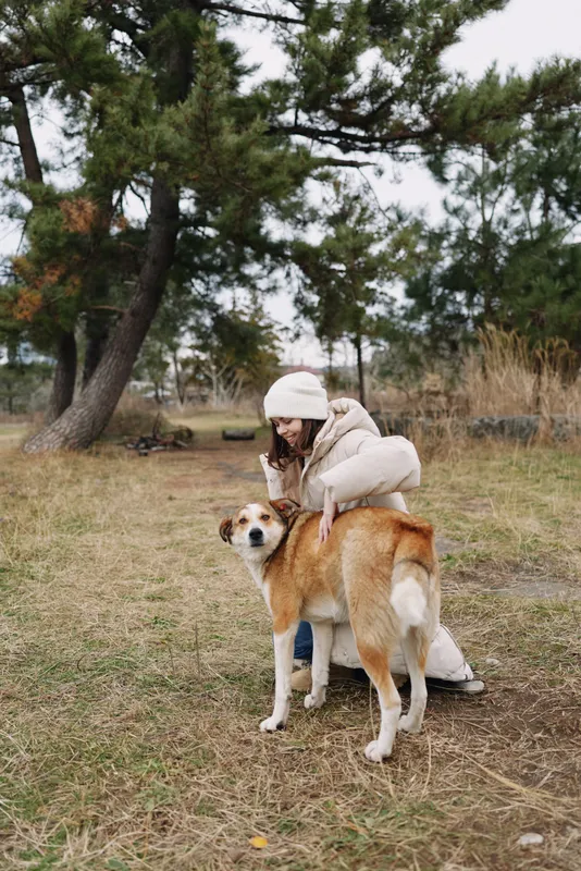 Dog, woman, outdoors, park, coat, winter companion in a quiet scene with a friendly dog near trees and grass, capturing gentle moments of companionship and care.