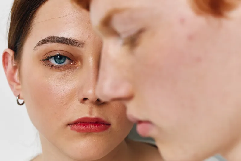 Closeup of young woman and man with serious expressions in studio with soft light, focus on eyes, skin texture and facial details in intimate portrait photography.