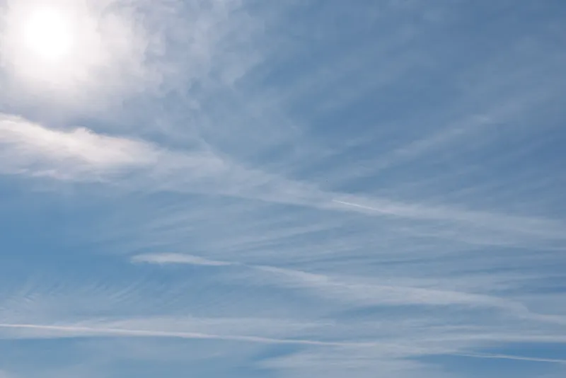 Blue sky with wispy clouds and a bright sun, a serene outdoor scene capturing daylight, gentle atmosphere, vast openness, and calm weather.