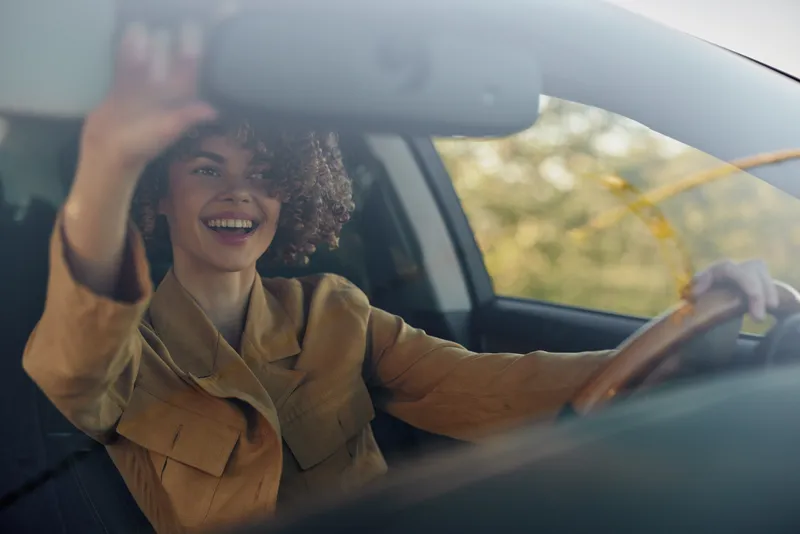 A joyful woman drives a car in a bright scene, captured with retro film color tones, depicting a casual lifestyle moment, optimism, and a sense of travel and freedom.