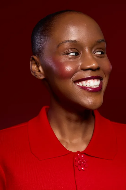 Close-up portrait of a smiling dark skinned African woman wearing red clothing against a red background. Concept of beauty, confidence, fashion, and positive emotions.