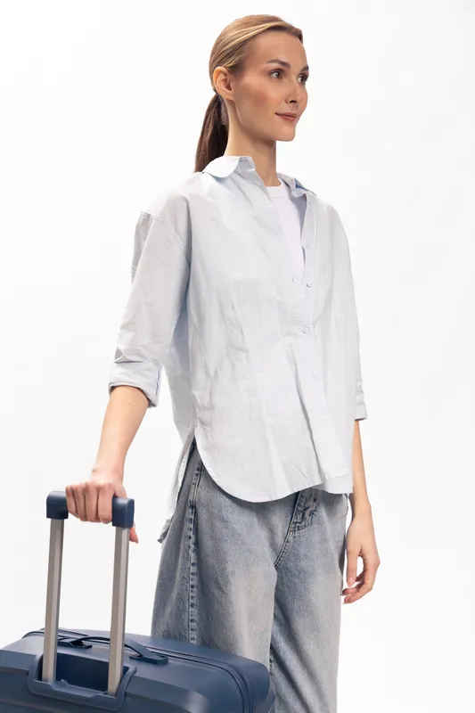 Young woman with suitcase stands in casual clothes, looking aside. Travel concept with luggage, preparation, and modern lifestyle on white background.
