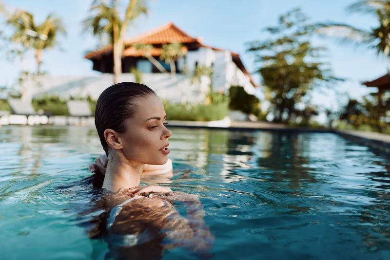Relaxed woman in a clear pool enjoys a sunny day, water ripples around her, serene mood, outdoor vacation scene, vivid blue surroundings, calm expression, leisure lifestyle, candid swim moment