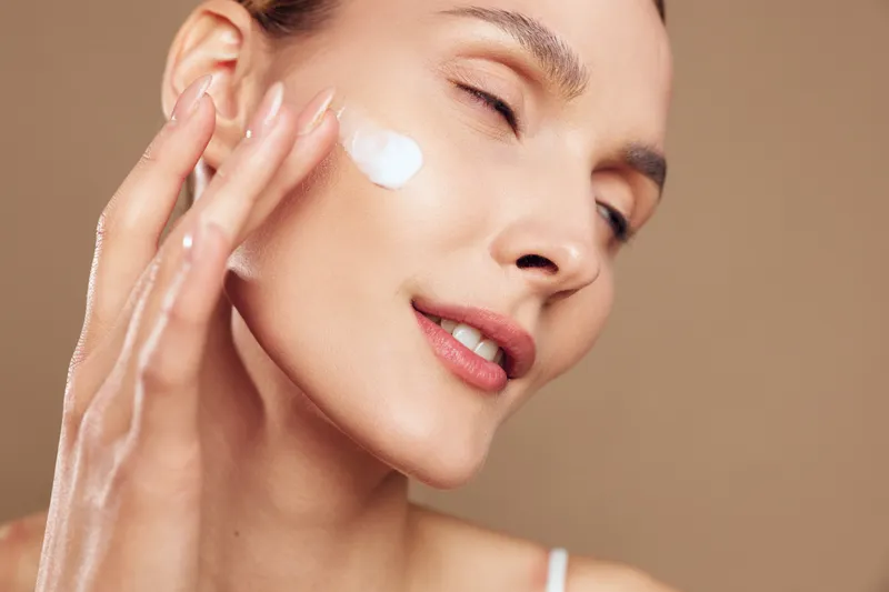 Skincare beauty woman face cream hydration spa wellness concept, eyes closed calm relaxation, hand on cheek applying moisturizer, smooth skin in soft studio light
