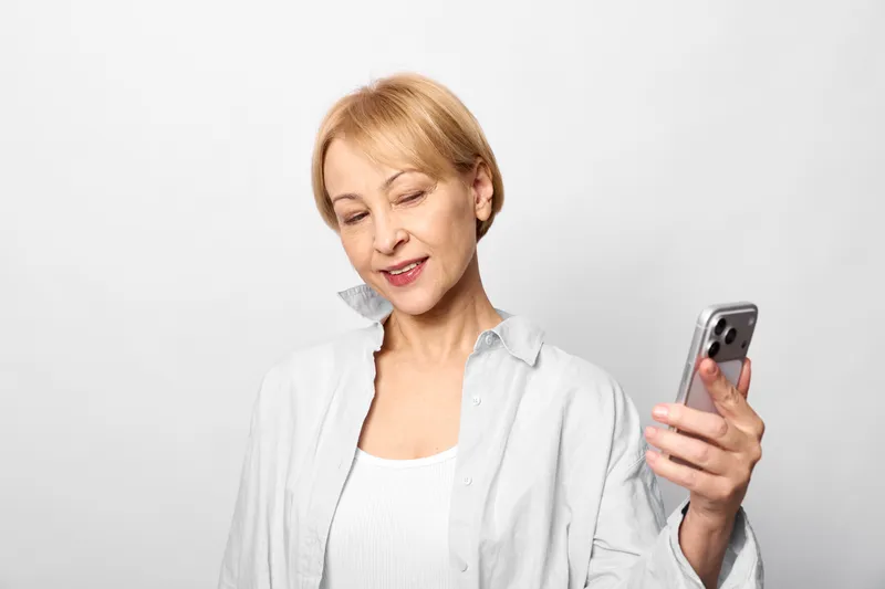 Woman with smartphone studio portrait, senior indoors, texting communication using technology on white background. Soft studio light and minimal space show calm everyday connectivity.