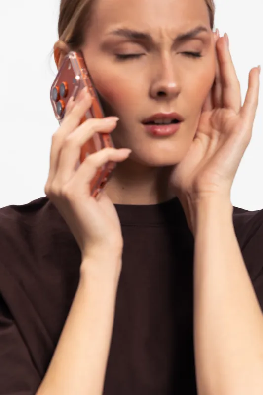 Stressed woman with closed eyes holds phone to ear and touches temple with hand. Facial expression shows discomfort or headache. Isolated on white background. Concept of stress and pain.