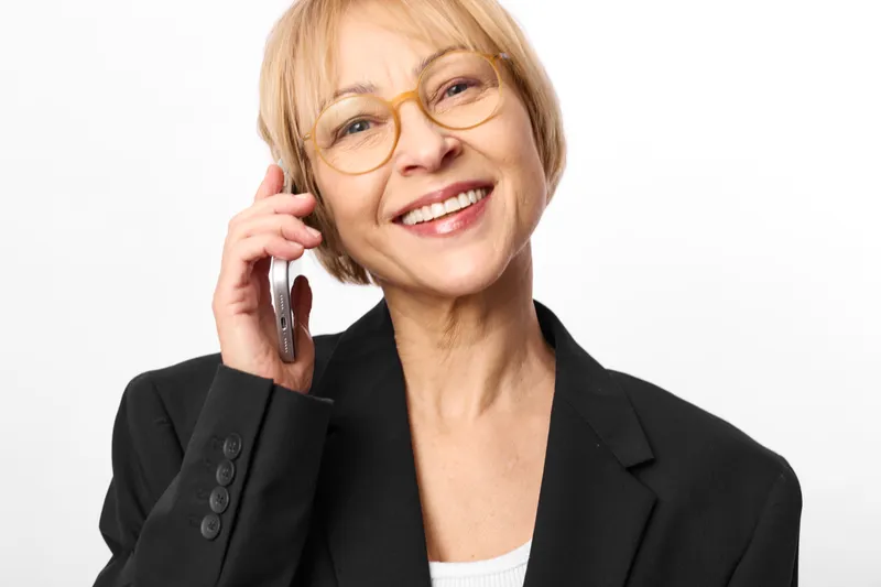 Blonde business woman with glasses holds a phone to her ear, smiling, friendly call, communication as a professional portrait on white background