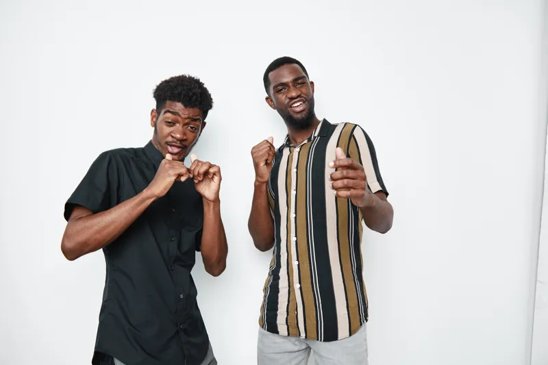 Two young black men with dark skin dancing and having fun together in casual clothes against white background. Friends enjoying music and positive mood indoors.
