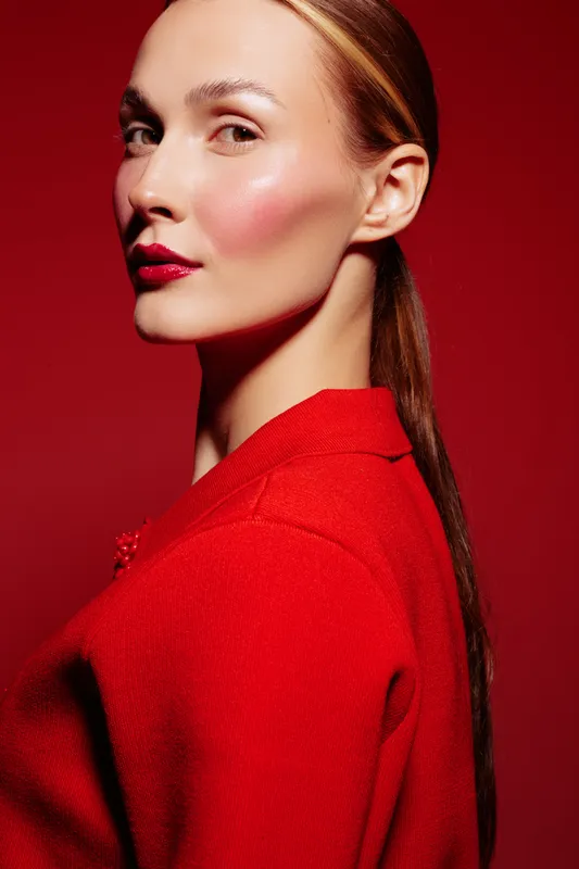 Portrait of a confident woman with sleek hair and red lipstick wearing a red outfit against a red background. Concept of fashion, beauty, elegance, and bold style in studio lighting.