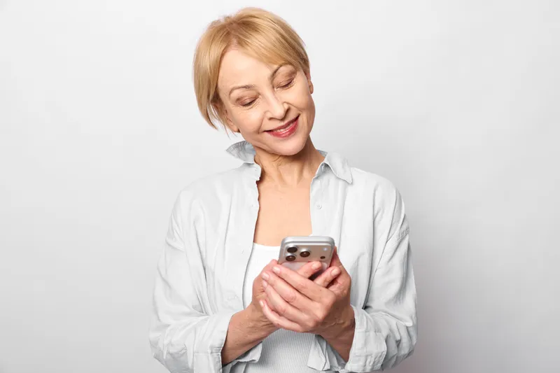 Elderly woman holds a smartphone, technology driven communication, social smile moment, studio portrait with digital screen view, calm hands on device
