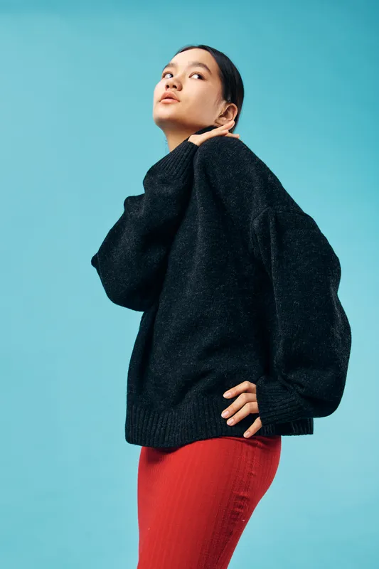 Young woman posing confidently in black sweater and red skirt against blue background, fashion portrait, casual style with modern outfit and expressive look for lifestyle content.