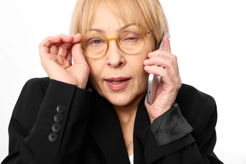 Elderly woman with glasses and phone communication for call, senior portrait in studio, business style, adjusting frames, calm expression, white background