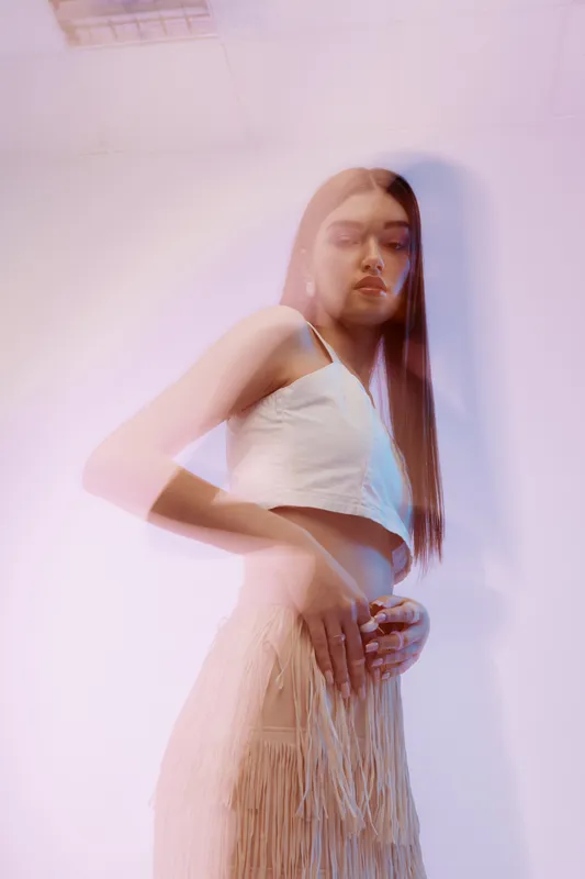 Young woman with long hair wearing a white top and beige skirt posing under soft pastel lighting. Concept of beauty, fashion, and modern style with artistic mood.