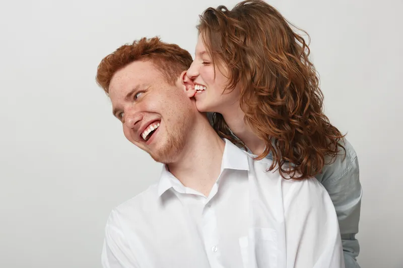 Happy young couple with red hair and curly hair laughing together on white background. Concept of love, friendship, joy, and positive emotions in relationships.