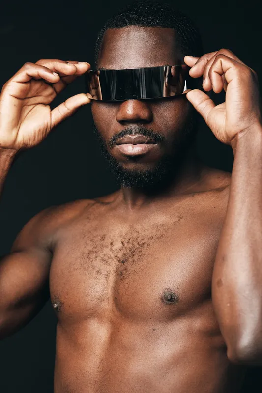 African man with dark skin and bare chest wearing futuristic visor glasses in creative conceptual visual style. Closeup portrait with modern technology and innovation theme on black background.