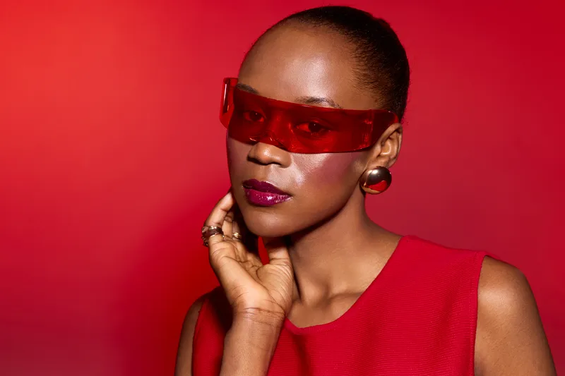 Portrait of a dark skinned African American woman wearing red sunglasses and a red top against a red background. Concept for fashion, style, beauty, and confident attitude.