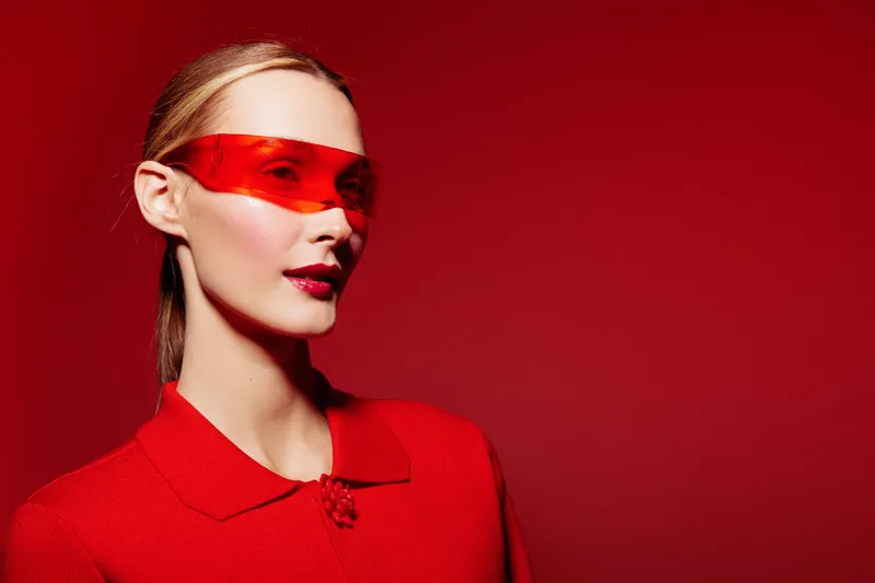 Portrait of a stylish woman wearing red sunglasses and a red outfit against a red background. Concept of fashion, modern style, and bold color contrast in studio lighting.