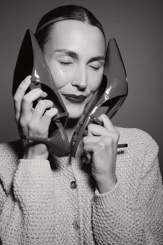 A happy Caucasian woman with fair skin holds two high heels near her face with closed eyes. Concept for fashion, style, elegance, and joyful emotions.